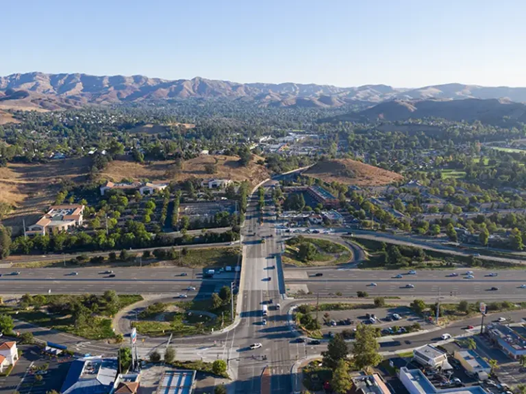 Aerial view of a highway interchange with surrounding suburban area and hills in the background.