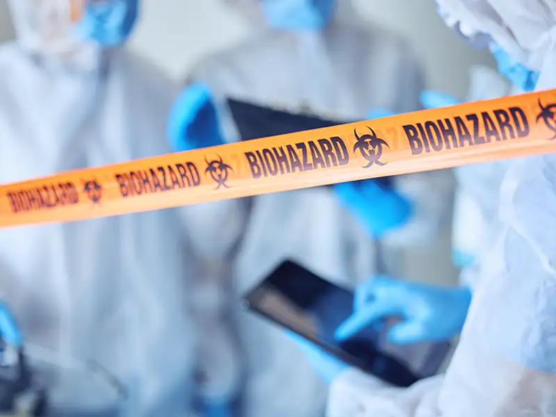Biohazard tape in front of people wearing protective suits and gloves.
