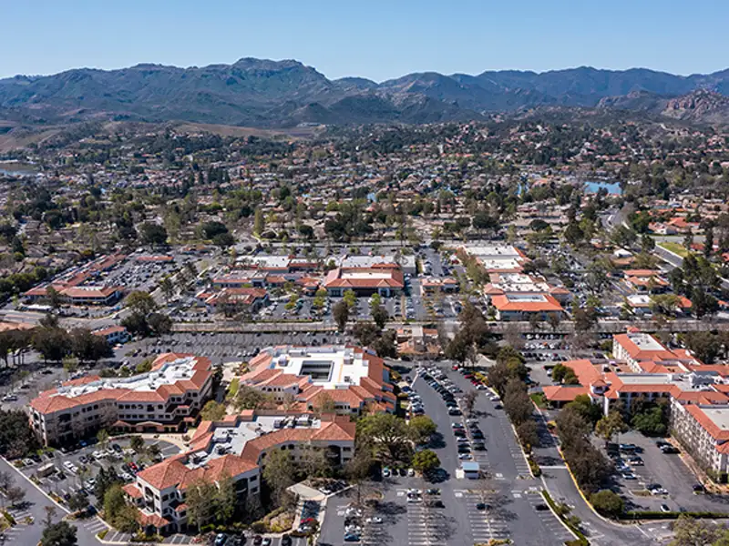 Aerial view of a suburban area with buildings, parking lots, and mountains in the background.