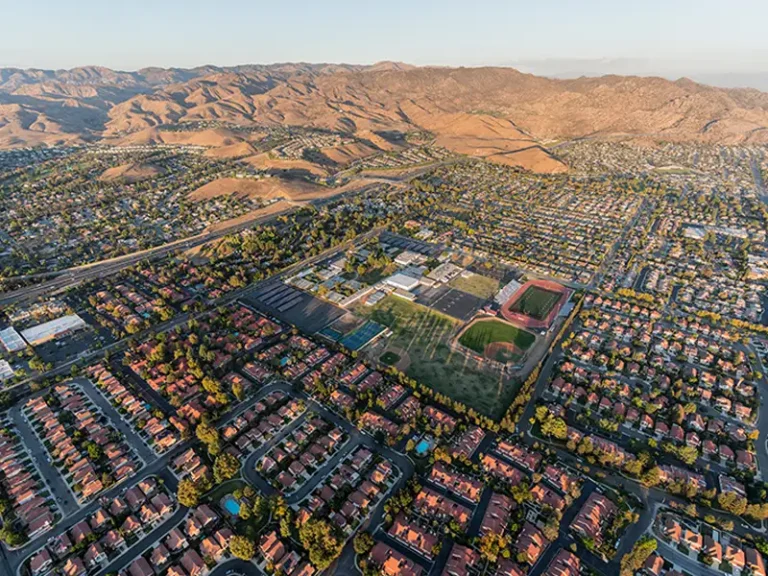 Aerial view of a suburban neighborhood surrounding a school with sports fields and mountains in the background.