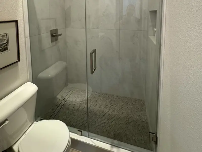 Small bathroom with a white toilet and a glass-enclosed shower with pebble flooring.
