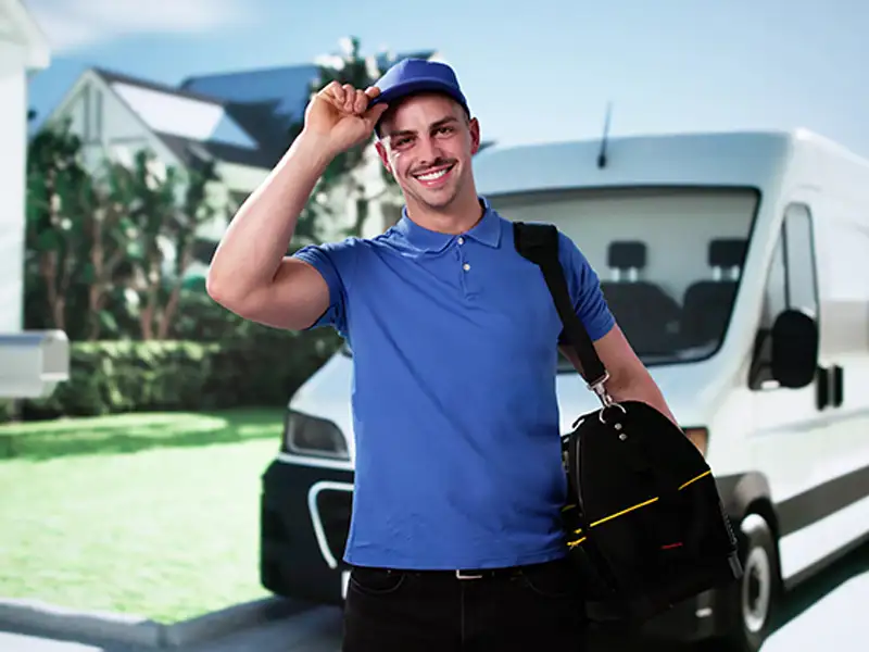 Delivery man in blue uniform tipping his cap, standing in front of a white van.