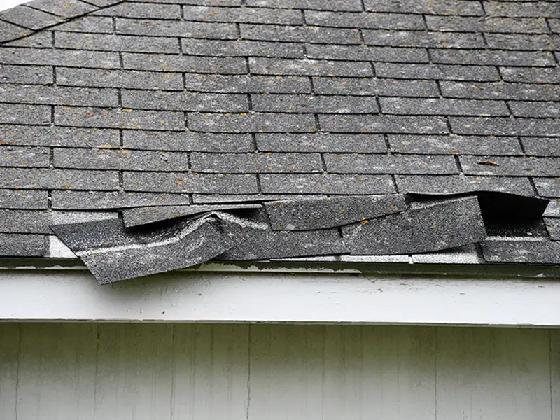 Damaged and curled asphalt roof shingles on a house edge.