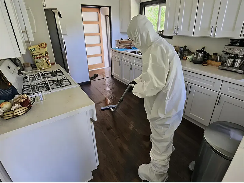 Person in white protective suit cleaning a kitchen floor with a mop.